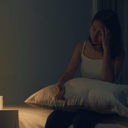Beautiful Asian young woman sitting on bed take sleeping pill or night medicine in bedroom. Unhealthy sick Indian female suffers from insomnia or headache, depressed girl holds antidepressant meds.