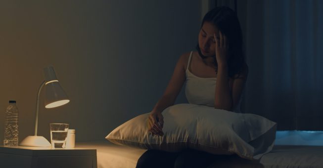 Beautiful Asian young woman sitting on bed take sleeping pill or night medicine in bedroom. Unhealthy sick Indian female suffers from insomnia or headache, depressed girl holds antidepressant meds.