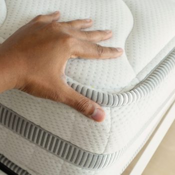 Hand touching and pressing orthopedic mattress on bed