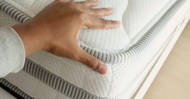Hand touching and pressing orthopedic mattress on bed
