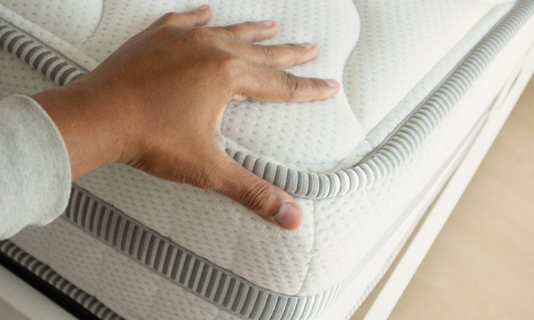 Hand touching and pressing orthopedic mattress on bed