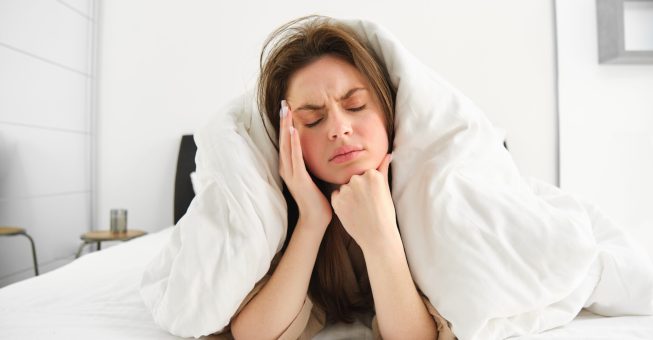 Portrait of woman rolled in blankets in bed, frowning and feeling unwell, has hangover, headache in morning, resting at home.