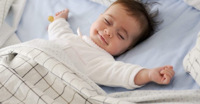 Smiling baby girl lying on a bed sleeping on blue sheets