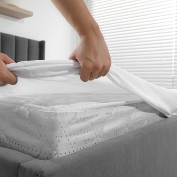 Woman covering mattress with protector indoors, closeup