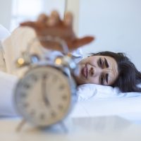 Woman lying in bed turning off an alarm clock in the morning at 5am. Hand turns off the alarm clock waking up at morning, girl turns off the alarm clock waking up in the morning from a call.