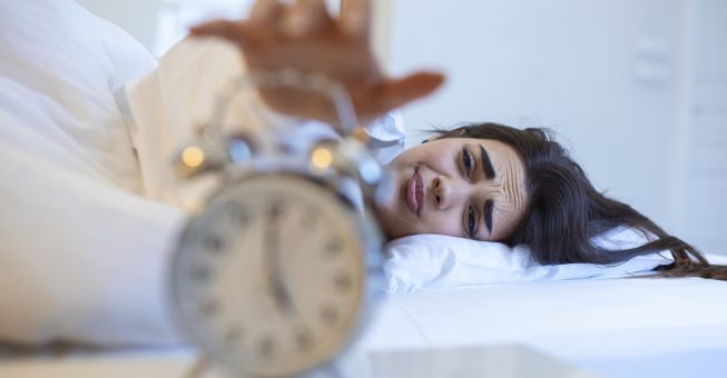 Woman lying in bed turning off an alarm clock in the morning at 5am. Hand turns off the alarm clock waking up at morning, girl turns off the alarm clock waking up in the morning from a call.