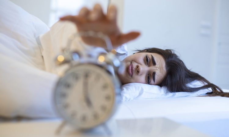 Woman lying in bed turning off an alarm clock in the morning at 5am. Hand turns off the alarm clock waking up at morning, girl turns off the alarm clock waking up in the morning from a call.