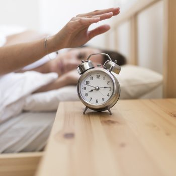woman-turning-off-alarm-clock-while-lying-bed
