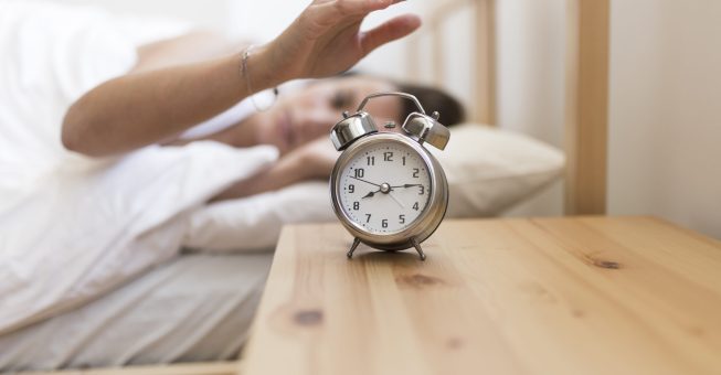 woman-turning-off-alarm-clock-while-lying-bed