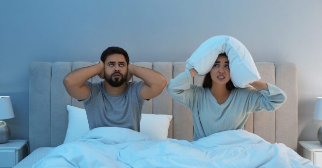 Young couple suffering from noisy neighbours in bed at home
