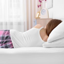 Young woman lying on bed with orthopedic pillow against blurred background. Healthy posture concept