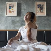 Young woman sitting on the bed with neck pain after wake up