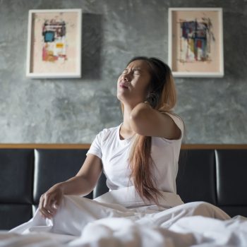 Young woman sitting on the bed with neck pain after wake up