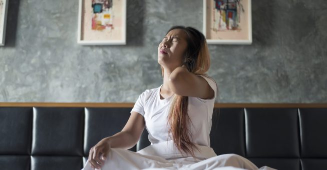 Young woman sitting on the bed with neck pain after wake up