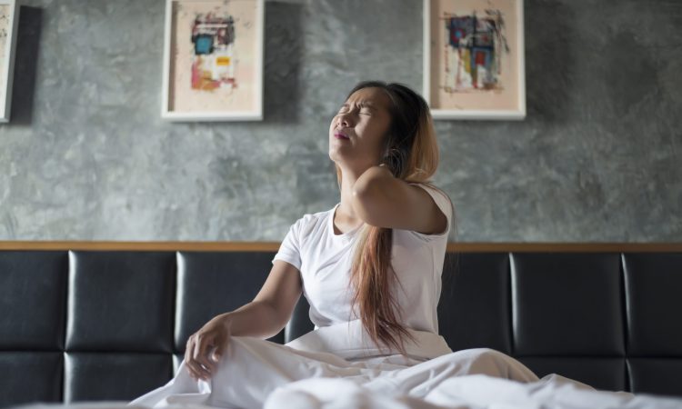 Young woman sitting on the bed with neck pain after wake up